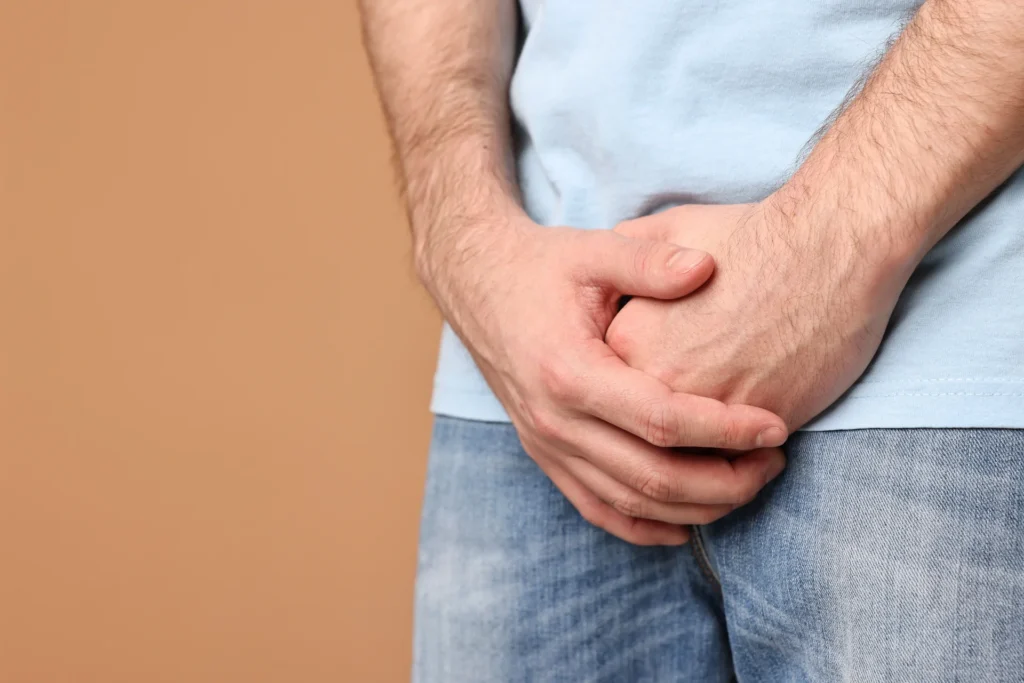 adult man holding groin in pain against brown back 2026 05 12 18 26 13 utc